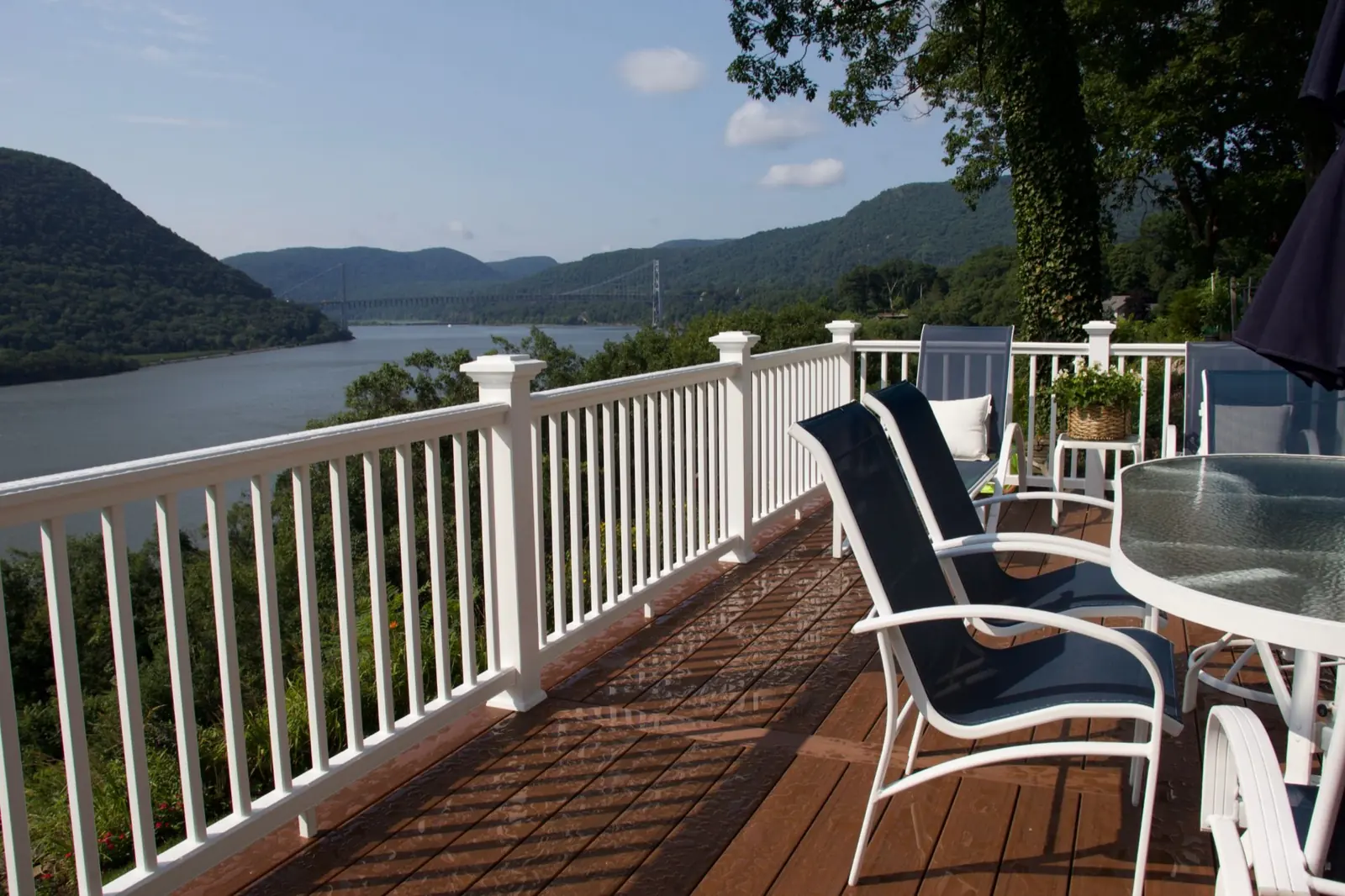 Composite deck with seating, a glass dining table, and white railings overlooking the Hudson River